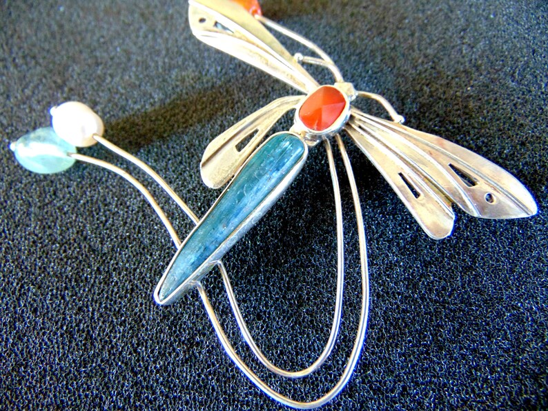 K&ouml;nnte beinhalten: Silberne Libellenbrosche mit blauen, gr&uuml;nen und roten Edelsteinen. Die Fl&uuml;gel der Libelle sind detailliert und kunstvoll gearbeitet.