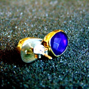 Peut inclure: Une boucle d'oreille en or avec une pierre pr&eacute;cieuse violette. La boucle d'oreille est de style clou avec une tige et un fermoir.