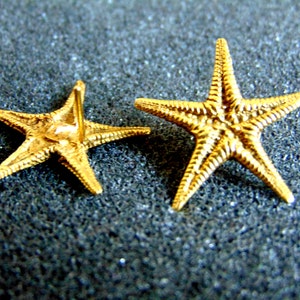 May include: A pair of gold-tone starfish earrings. The earrings are made of metal and have a simple, elegant design.
