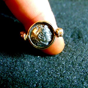 K&ouml;nnte beinhalten: Ein goldener Ring mit einer silbernen M&uuml;nze in der Mitte. Die M&uuml;nze zeigt das Profil eines Kopfes.