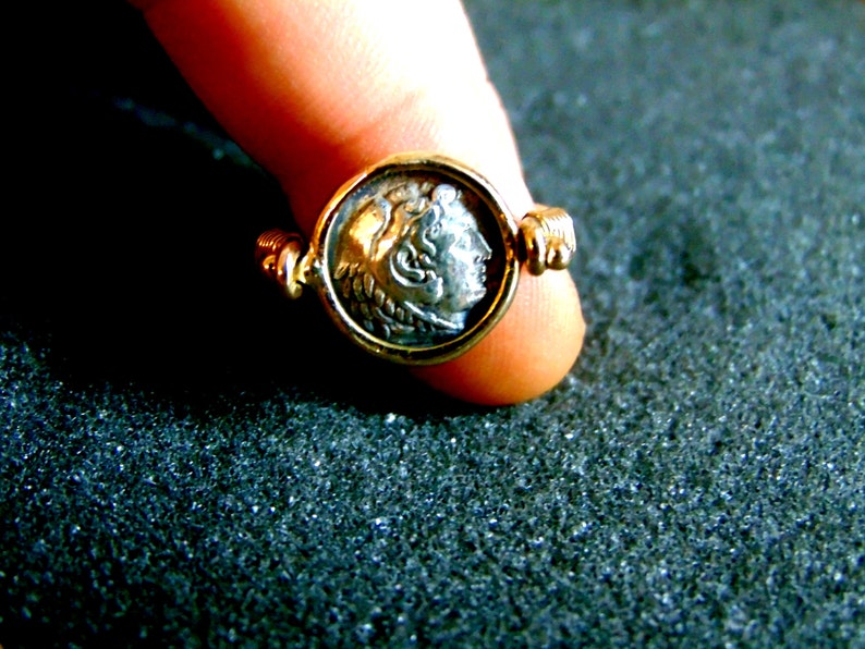 K&ouml;nnte beinhalten: Ein goldener Ring mit einer silbernen M&uuml;nze in der Mitte. Die M&uuml;nze zeigt das Profil eines Kopfes.