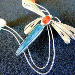 K&ouml;nnte beinhalten: Silberne Libellenbrosche mit blauen, gr&uuml;nen und roten Edelsteinen. Die Fl&uuml;gel der Libelle sind detailliert und kunstvoll gearbeitet.