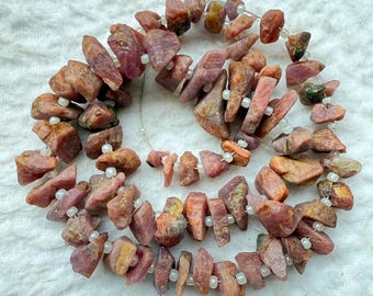 May include: Strung gemstone beads in shades of pink, brown, and yellow. The beads are irregular in shape and size, with a few small white beads interspersed. The text "RJ-6" and "19X8 MM" are visible.