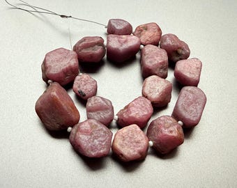 May include: A strand of rough-cut, pinkish-red gemstone beads. The beads are irregularly shaped and strung together with a thin, silver-colored wire. The gemstones have a natural, unpolished appearance.