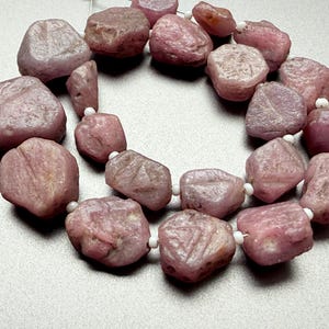 Puede incluir: Collar de piedras preciosas rosas en bruto. Las piedras son de forma y tamaño irregulares, ensartadas con cuentas blancas. Las piedras preciosas tienen un aspecto natural, sin pulir, con variaciones de color y textura. Ideal para la creación de joyas.