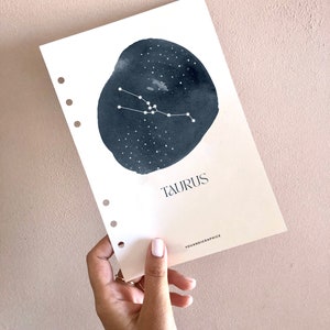 Puede incluir: Una página de planificador imprimible blanca con un círculo de acuarela negro que presenta la constelación de Tauro y la palabra "TAURUS" en texto negro. El texto "YOUANDIGRAPHICS" está en la esquina inferior derecha.