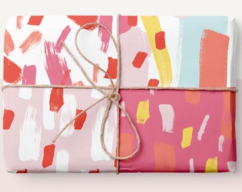 Könnte beinhalten: Eine Geschenkbox, verpackt in buntes, abstrakt gemustertes Papier mit rosa, roten, gelben und blauen Pinselstrichen. Die Box ist mit Schnur gebunden.