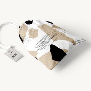 May include: A white drawstring bag with a black and beige abstract pattern. The bag has a white tag with the text "TO RN" on it.