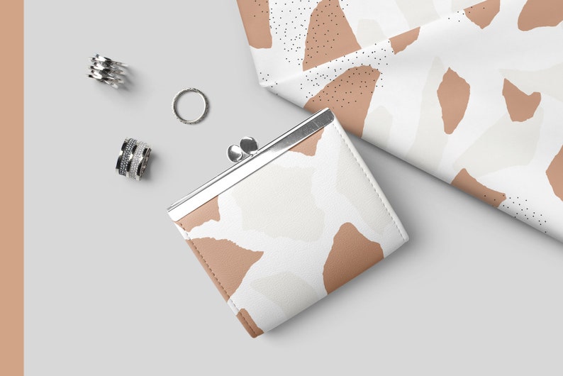 May include: A small, white and brown patterned coin purse with a silver clasp. The purse is lying on a white surface with silver rings nearby.