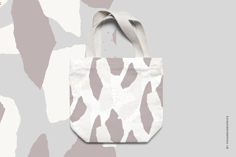 May include: A white tote bag with a pattern of abstract shapes in shades of gray and white. The bag has a white canvas strap.