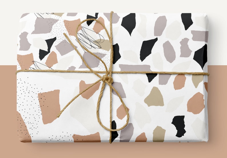 May include: A white gift box wrapped in paper with a terrazzo pattern in shades of brown, beige, gray, and black. The box is tied with a brown twine bow.