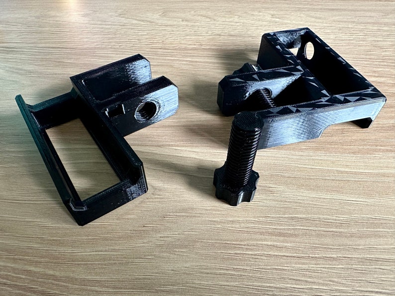 May include: Black 3D-printed mechanical components, including a bracket, a frame, and a bolt. The bracket has a rectangular opening and a threaded hole. The bolt has a hexagonal head. The components are designed for mechanical assembly.