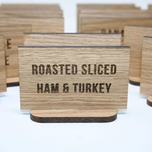May include: Wooden sign with the text "Roasted Sliced Ham & Turkey" in a rustic font. The sign is made of light brown wood and has a dark brown base.