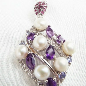 May include: A silver necklace with a pendant featuring a cluster of white pearls and purple amethyst gemstones. The pendant is shaped like a leaf and has a small red ruby gemstone at the top.