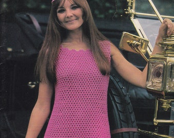 May include: A woman wearing a pink crochet dress with a scalloped hem. She is standing next to a vintage car.
