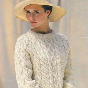 May include: A cream-coloured cable knit jumper with a round neckline. The jumper features a classic cable knit pattern and is made from a soft, warm yarn.
