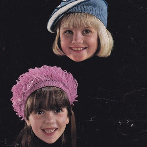 May include: Three girls wearing different styles of knitted hats. The first girl is wearing a blue and white striped beret, the second girl is wearing a pink crocheted hat with a ruffled edge, and the third girl is wearing a white crocheted beret.
