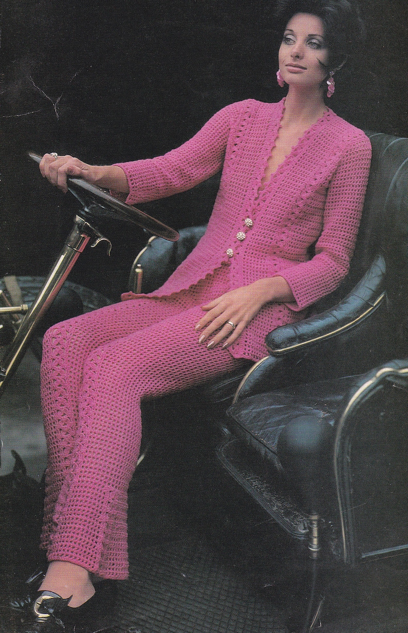 May include: A woman wearing a pink crocheted pantsuit with a V-neckline and button closures. She is sitting in a black leather chair with a gold trim.