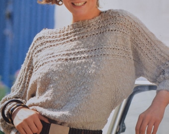Puede incluir: Un suéter de punto beige con un delicado patrón de encaje. El suéter tiene un cuello redondo y mangas largas. La modelo lleva un cinturón marrón con una hebilla plateada.