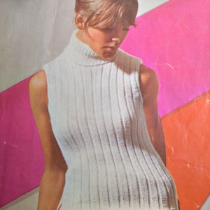 May include: A white sleeveless turtleneck sweater with a ribbed texture. The sweater is worn by a model with a bouffant hairstyle.