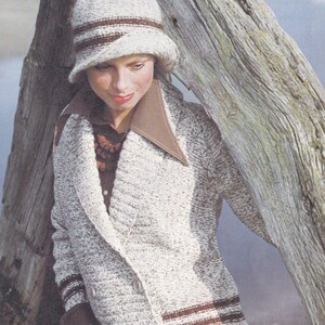 May include: A woman wearing a white and brown knitted cardigan with a brown collar and brown stripes on the sleeves. She is wearing a brown and white knitted hat with a brown band.