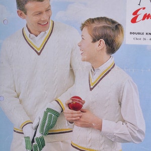 May include: Two people wearing white cable knit vests with brown, yellow, and white stripes. The vests have a V-neck and are worn over white shirts. The person on the left is holding a cricket bat and a green cricket glove. The person on the right is holding a red cricket ball. The image includes the text "DOUBLE KNIT Chest 26-4"