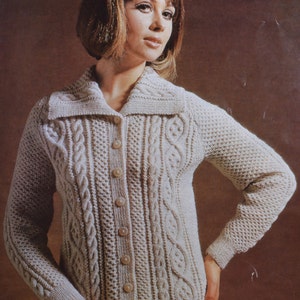 Peut inclure: Un cardigan blanc en tricot avec un motif en câble et un grand col. Le cardigan a une fermeture boutonnée à l'avant et des manches longues.