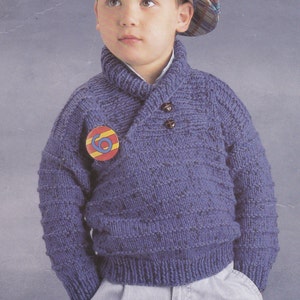 May include: A blue knitted jumper with a collared neckline and two buttons. The jumper has a textured pattern and a small round badge with the number "6" on it.