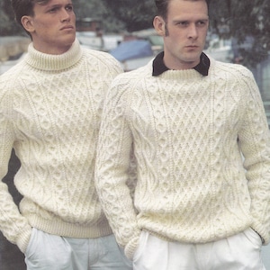 May include: Two men wearing white cable knit sweaters. The sweater on the left has a turtleneck collar. The sweater on the right has a round neckline.