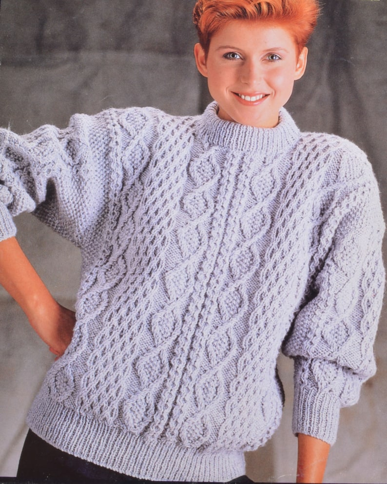 May include: A light purple cable knit sweater with a round neckline. The sweater has a textured pattern of woven cables.