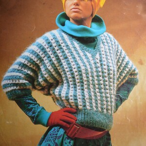 May include: A teal and white striped sweater with a v-neck and a turtleneck collar. The sweater is made of a soft, fuzzy yarn and has a loose fit.