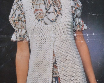 May include: A white crocheted vest with a long, open front. The vest has a geometric pattern and is worn over a patterned dress.
