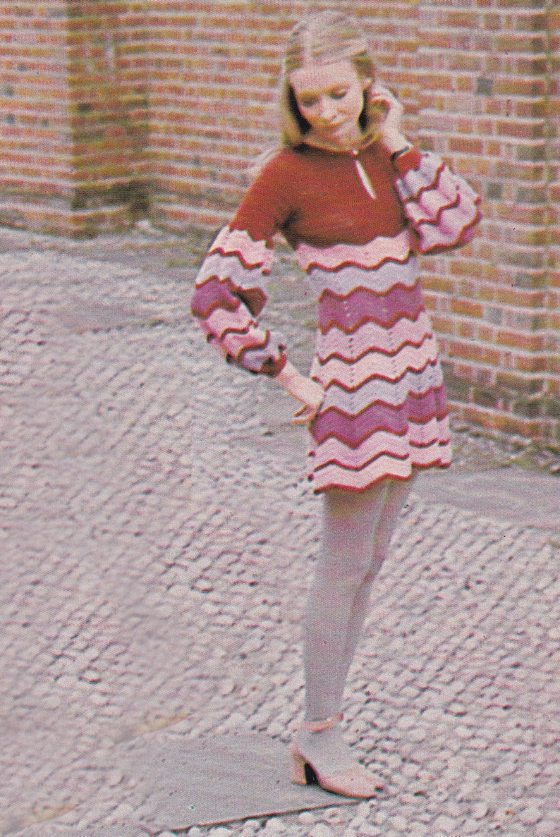 May include: A pink and purple striped crochet dress with long sleeves and a high neckline. The dress is being worn by a person with long blonde hair.