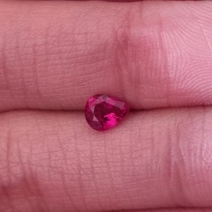 Può includere: Una gemma di rubino sfaccettata a forma di cuore. La gemma è di un colore rosso intenso e vibrante e sembra essere tenuta in una mano. Le sfaccettature del rubino catturano la luce, creando un effetto scintillante. Adatto per la creazione di gioielli.