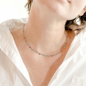 May include: A silver chain necklace with small turquoise and red beads.