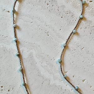 May include: A delicate necklace with a brown cord and light blue beads. The necklace has a gold clasp.