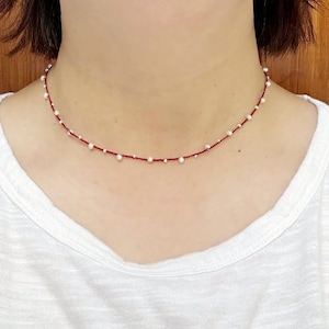 May include: A delicate red and white pearl necklace with small white pearls spaced evenly along a thin red string.