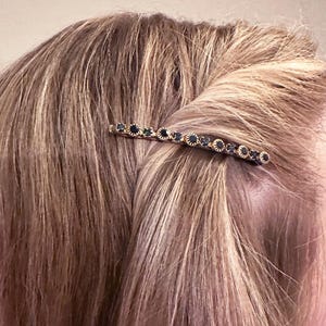 May include: A gold hair clip with black rhinestones. The clip is curved and has a row of rhinestones down the center.