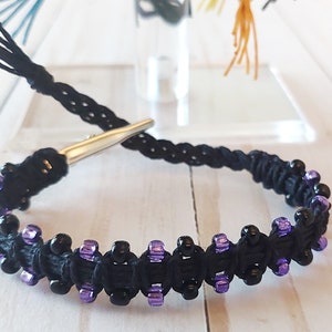 Puede incluir: Pulsera de cordón negro con cuentas negras y moradas y cierre plateado.