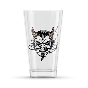 May include: A clear glass pint glass with a black and white illustration of a devil's face with red horns and a cigarette in its mouth.