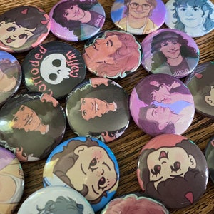 May include: A collection of colorful round pins with various designs. Some pins feature cartoon characters, others have skull and crossbones, and some have text like "Corroded Coffin".