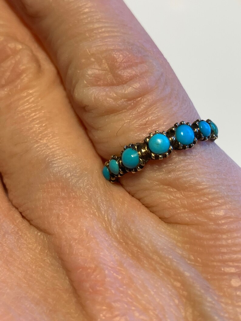 May include: A gold ring with a row of turquoise stones set in a bezel setting.