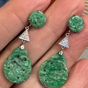 May include: A pair of dangle earrings with green jade and diamond accents. The jade is carved with floral designs and the diamonds are set in a triangular shape.