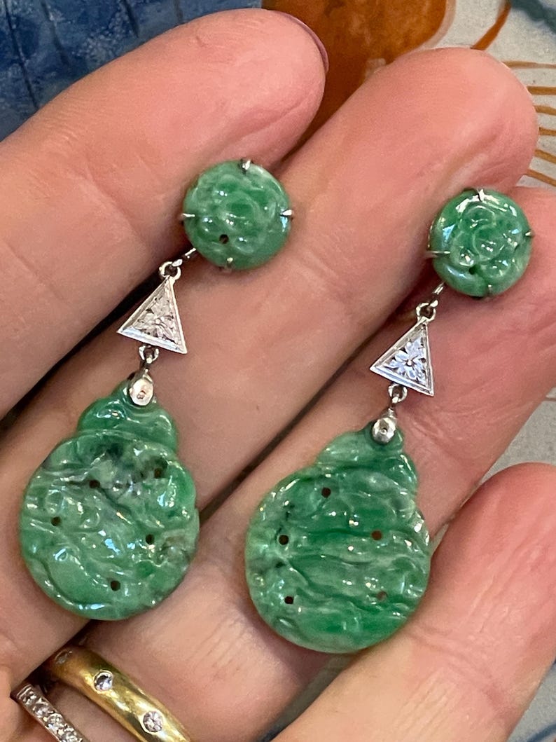 May include: A pair of dangle earrings with green jade and diamond accents. The jade is carved with floral designs and the diamonds are set in a triangular shape.