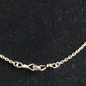 May include: A gold chain necklace with a small, dark grey gemstone at the clasp.