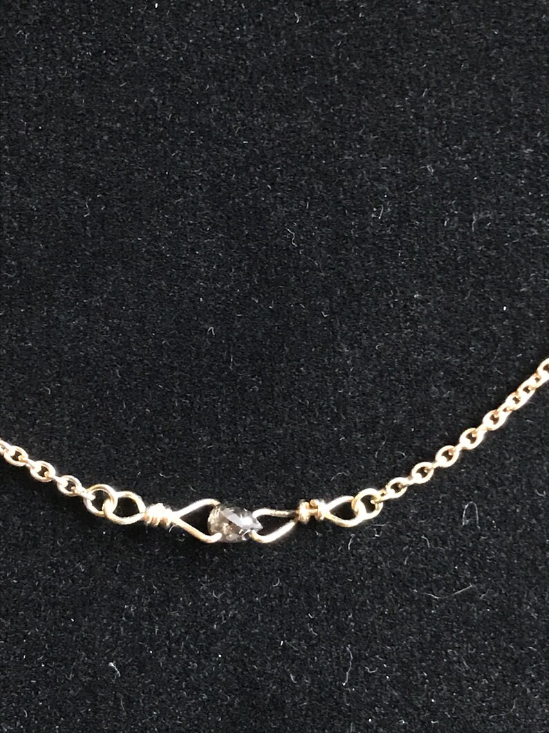 May include: A gold chain necklace with a small, dark grey gemstone at the clasp.