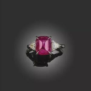 May include: A ring featuring a large, rectangular, deep pink ruby. Two smaller, triangular, clear gemstones are set either side of the main stone. The ring is set in a dark metal, against a black background.