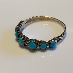 May include: A silver ring with a row of turquoise stones set in the band.