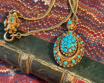 May include: A gold chain necklace with a pendant featuring a cluster of turquoise stones set in a gold frame. The necklace is lying on a book with a marbled cover.