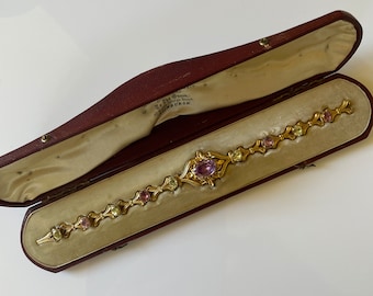May include: A gold bracelet with a delicate design featuring alternating oval-shaped amethyst and green stones. The bracelet is in a red velvet box with the inscription "The Queen, 12, Bridge Street, GLASGOW."